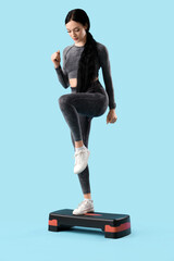Portrait of sporty young woman exercising with stepper on blue background