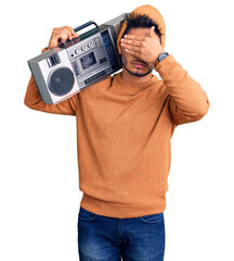 Handsome latin american young man holding boombox, listening to music covering eyes with hand,...