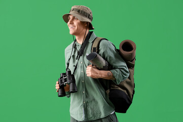 Fototapeta premium Male traveler with binoculars on green background