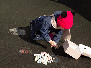 child draws with chalk on the playground on a spring day