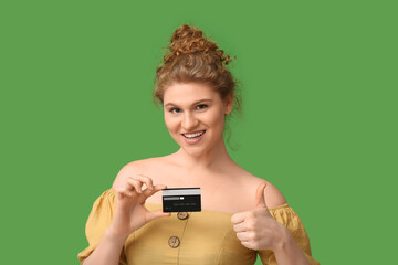 Beautiful young woman with credit card showing thumb-up gesture on green background