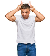 Handsome muscle man wearing casual white tshirt posing funny and crazy with fingers on head as bunny ears, smiling cheerful