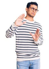 Hispanic handsome young man wearing casual clothes and glasses disgusted expression, displeased and fearful doing disgust face because aversion reaction. with hands raised