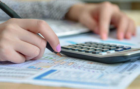 manos de mujer con u&ntilde;as pintadas de rosa, cogiendo un boligrafo y realizando tareas con documentos fiscales en mesa con una calculadora