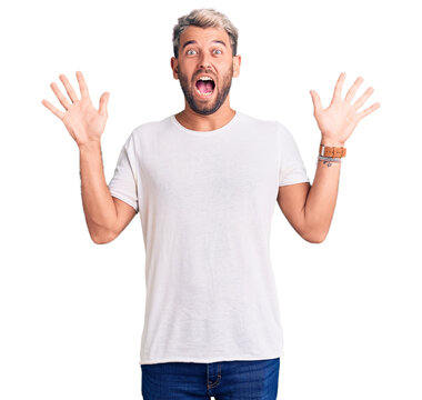 Young handsome blond man wearing casual t-shirt pointing fingers to camera with happy and funny face. good energy and vibes.