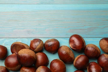  Roasted edible sweet chestnuts on light blue wooden table, flat lay. Space for text © New Africa