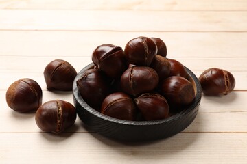Plate with roasted edible sweet chestnuts on wooden table, closeup