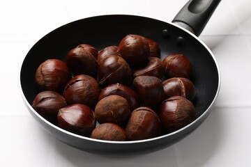 Fresh edible sweet chestnuts in frying pan on white tiled table