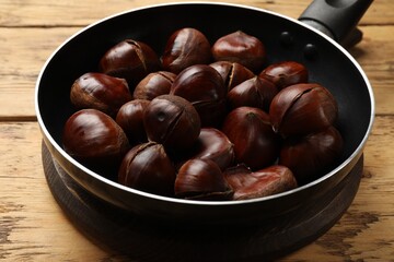 Fresh edible sweet chestnuts in frying pan on wooden table, closeup