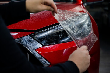 The master applies vinyl film to the headlight of a red car. 
