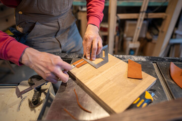 Male hands cutting leather skin. Master measures right amount, uses caliper and construction knife, makes leather covers for the bed legs to prevent them from scratching floor.