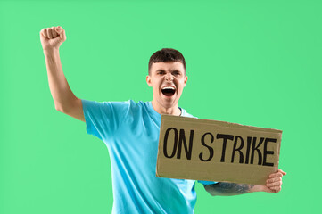 Protesting young man holding placard with text ON STRIKE against green background