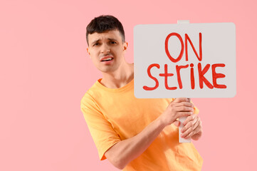 Protesting young man holding placard with text ON STRIKE against pink background