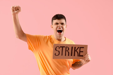 Protesting young man holding placard with word STRIKE against pink background