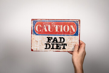 Fad Diet. Metal warning sign in a woman's hand on a white background - 780914414