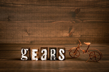 GEARS. Text from alphabet blocks and rusty miniature bicycle on wood texture background - 780914491