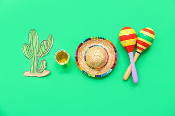 Maracas, paper cactus, decorative sombrero hat and shot of tequila on green background