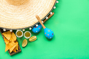 Sombrero, maracas, lime, nachos and shots of tequila on green background