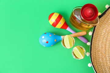 Composition with maracas, sombrero hat, lime, bottle and shots of tequila on green background