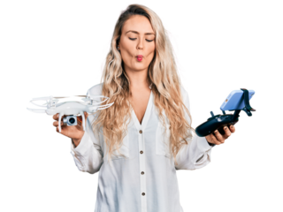 Young blonde woman holding television remote control making fish face with mouth and squinting eyes, crazy and comical.