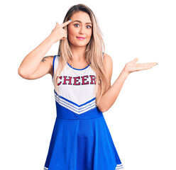 Young beautiful blonde woman wearing cheerleader uniform confused and annoyed with open palm...