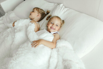 Two Young Children Laying on White Fluffy Bed