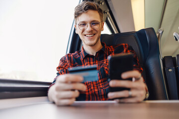 Passenger is using credit card and phone in train for online shopping.