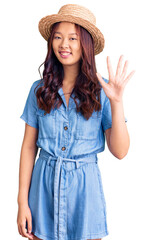 Obraz na płótnie Canvas Young beautiful chinese girl wearing summer hat showing and pointing up with fingers number five while smiling confident and happy.