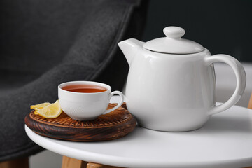 Board with cup of hot brewed tea, slices of lemon and pot on table against black blurred background