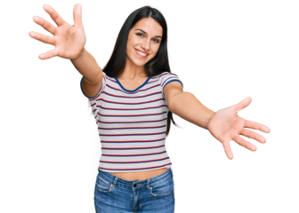 Young hispanic girl wearing casual striped t shirt looking at the camera smiling with open arms for hug. cheerful expression embracing happiness.