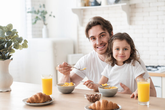 Young caring caucasian father feeding his small daughter with corn flakes in the morning for breakfast, family time, parenthood and fatherhood. Happy father`s day! I love you, dad!