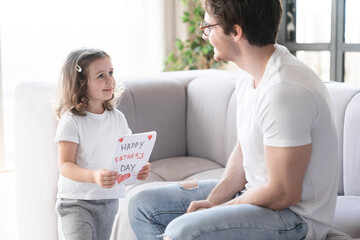 Smiling loving caring little kid daughter giving her young father greeting card, gift, present for...