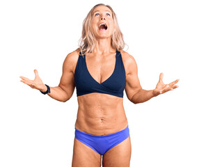 Middle age fit blonde woman wearing bikini crazy and mad shouting and yelling with aggressive...