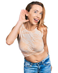 Young caucasian woman wearing casual style with sleeveless shirt smiling with hand over ear listening and hearing to rumor or gossip. deafness concept.