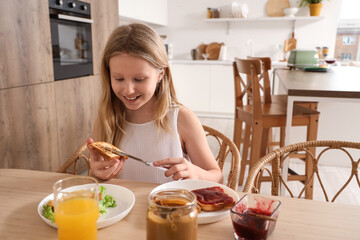 Little girl making toast with peanut butter at table in kitchen