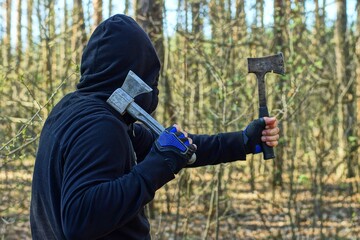 two small iron old sharp dangerous hatchets are held in the hands of an aggressive man dressed in a...