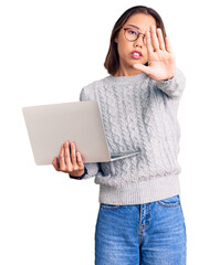 Young beautiful chinese girl wearing glasses holding laptop with open hand doing stop sign with serious and confident expression, defense gesture