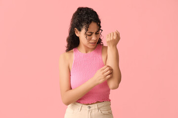 Young African-American woman with skin allergy scratching herself on pink background