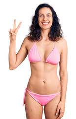 Young beautiful hispanic woman wearing bikini showing and pointing up with fingers number two while smiling confident and happy.