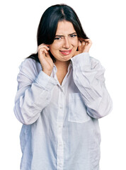 Beautiful hispanic woman wearing casual white shirt covering ears with fingers with annoyed expression for the noise of loud music. deaf concept.