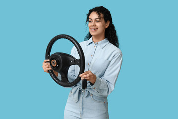 Beautiful young African-American woman with steering wheel and car key on blue background