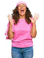 Fototapeta na wymiar Middle age hispanic woman wearing breast cancer support pink scarf celebrating mad and crazy for success with arms raised and closed eyes screaming excited. winner concept