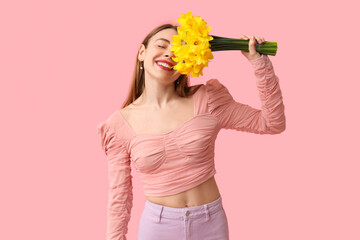 Happy young woman with bouquet of beautiful daffodil flowers on pink background