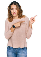 Beautiful young caucasian woman wearing casual sweater pointing aside worried and nervous with both...
