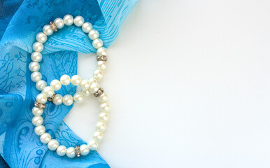 Two ivory faux pearls bracelets on top of blue fabric, white background with space for copy