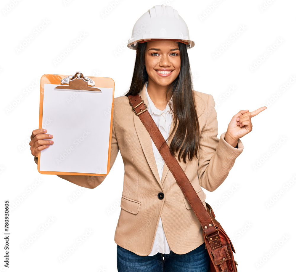 Wall mural Beautiful hispanic woman architect showing black space on clipboard smiling happy pointing with hand and finger to the side