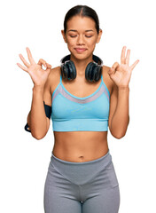 Beautiful hispanic woman wearing sportswear and headphones relax and smiling with eyes closed doing meditation gesture with fingers. yoga concept.