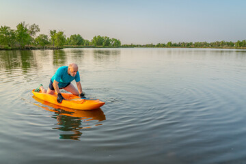 athletic, senior man is paddling a prone kayak on a lake in Colorado, this water sport combines aspects of kayaking and swimming - 780931619