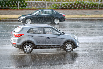 Cars driving fast through rain storm on city road, bad visibility. Car driving on flooded road,...