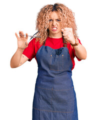 Young blonde woman with curly hair wearing barber apron annoyed and frustrated shouting with anger, yelling crazy with anger and hand raised